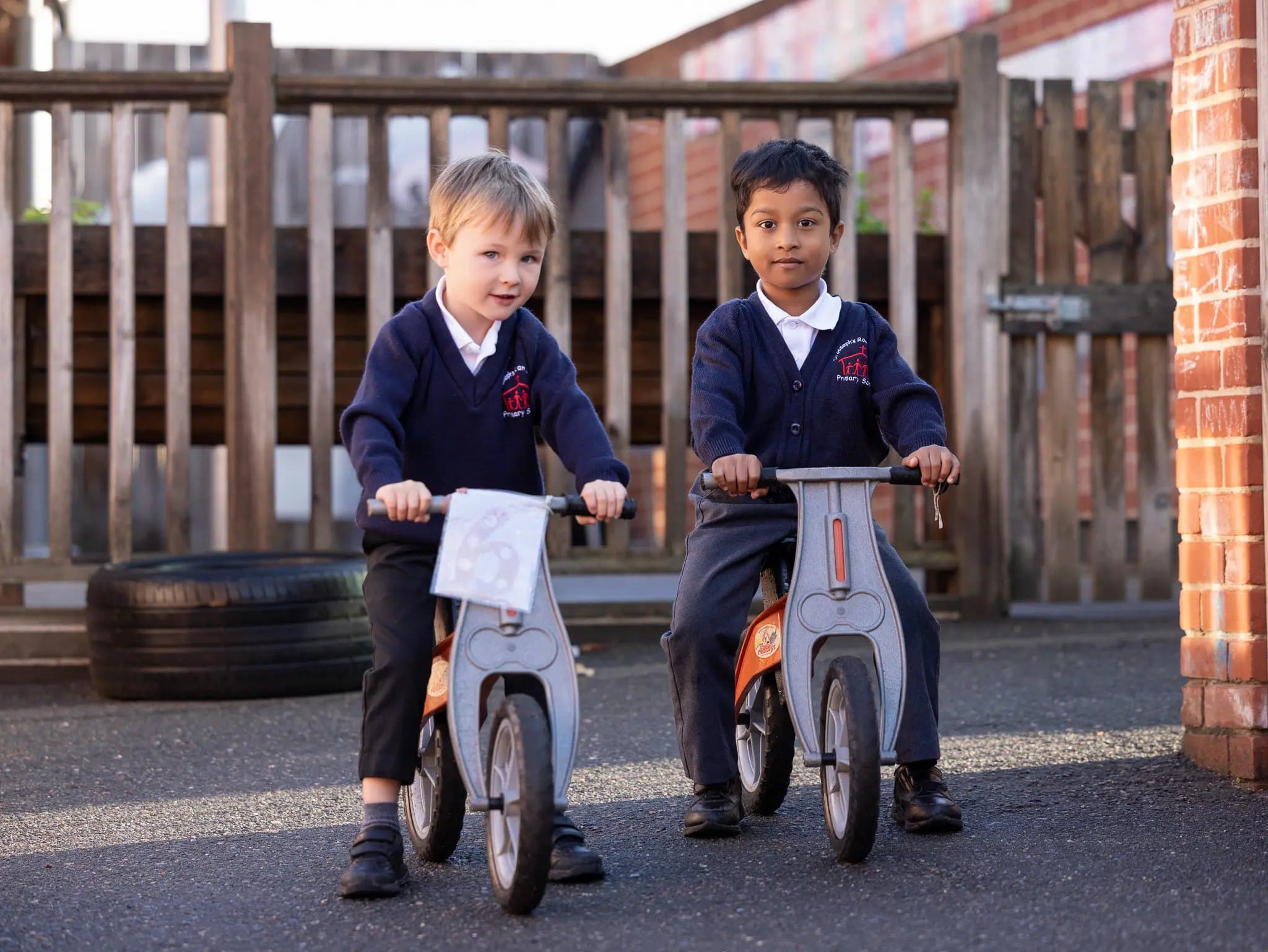 Two Reception children on balance bikes in the playground