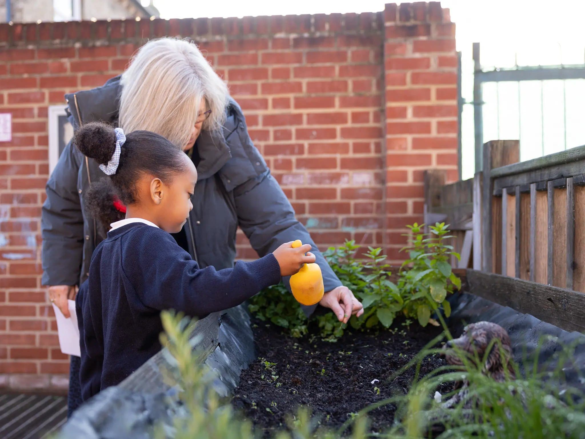 A pupil watering plants in the school garden with a member of staff