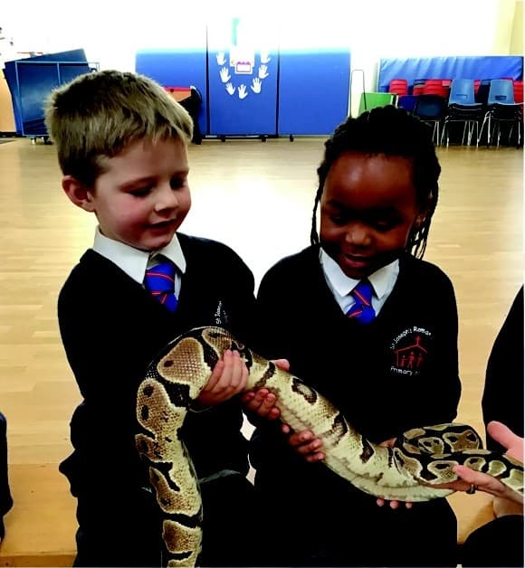 Two young pupils gently holding a snake during a visit