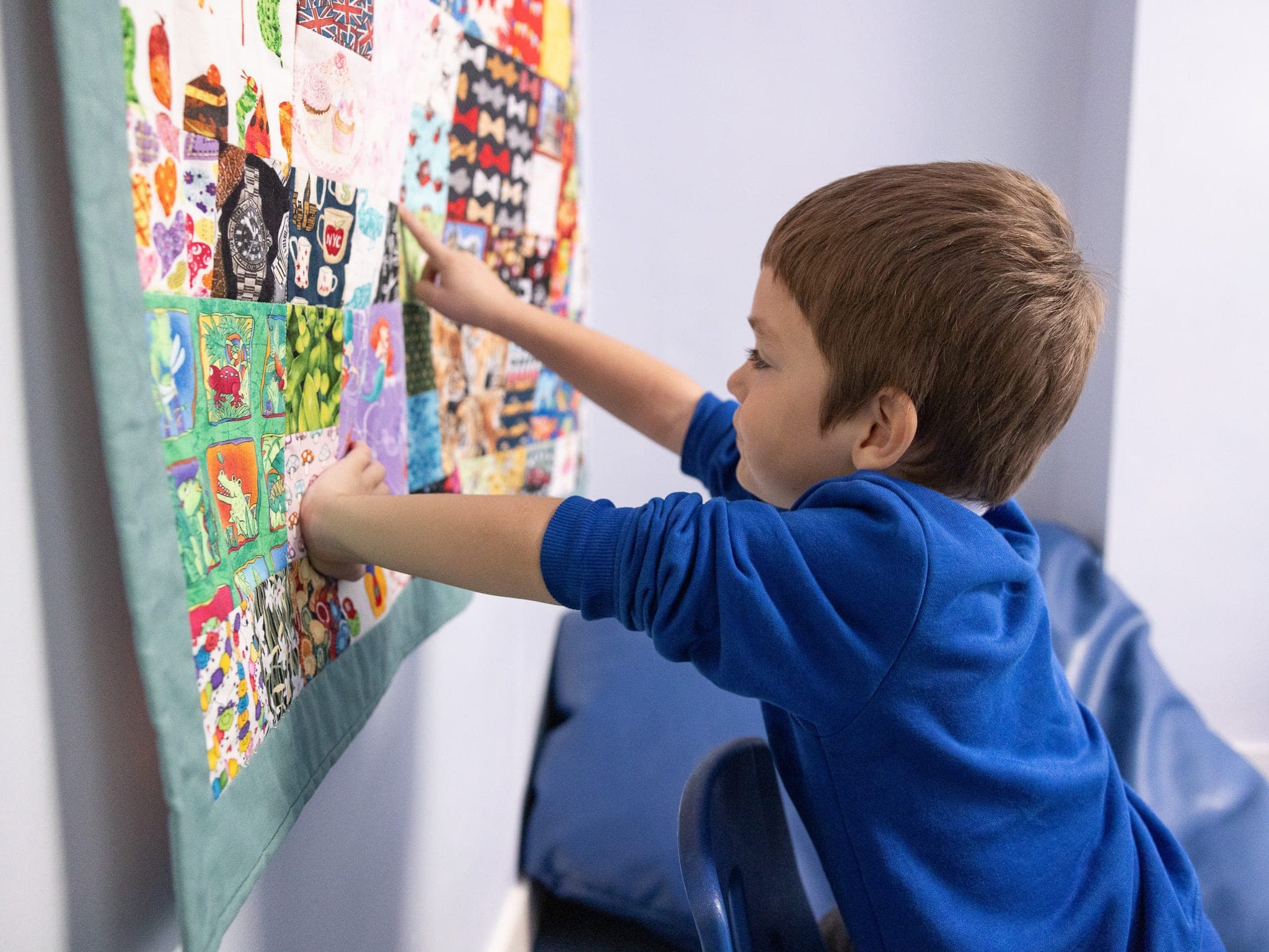 A boy pointing at a colourful patchwork display on the classroom wall