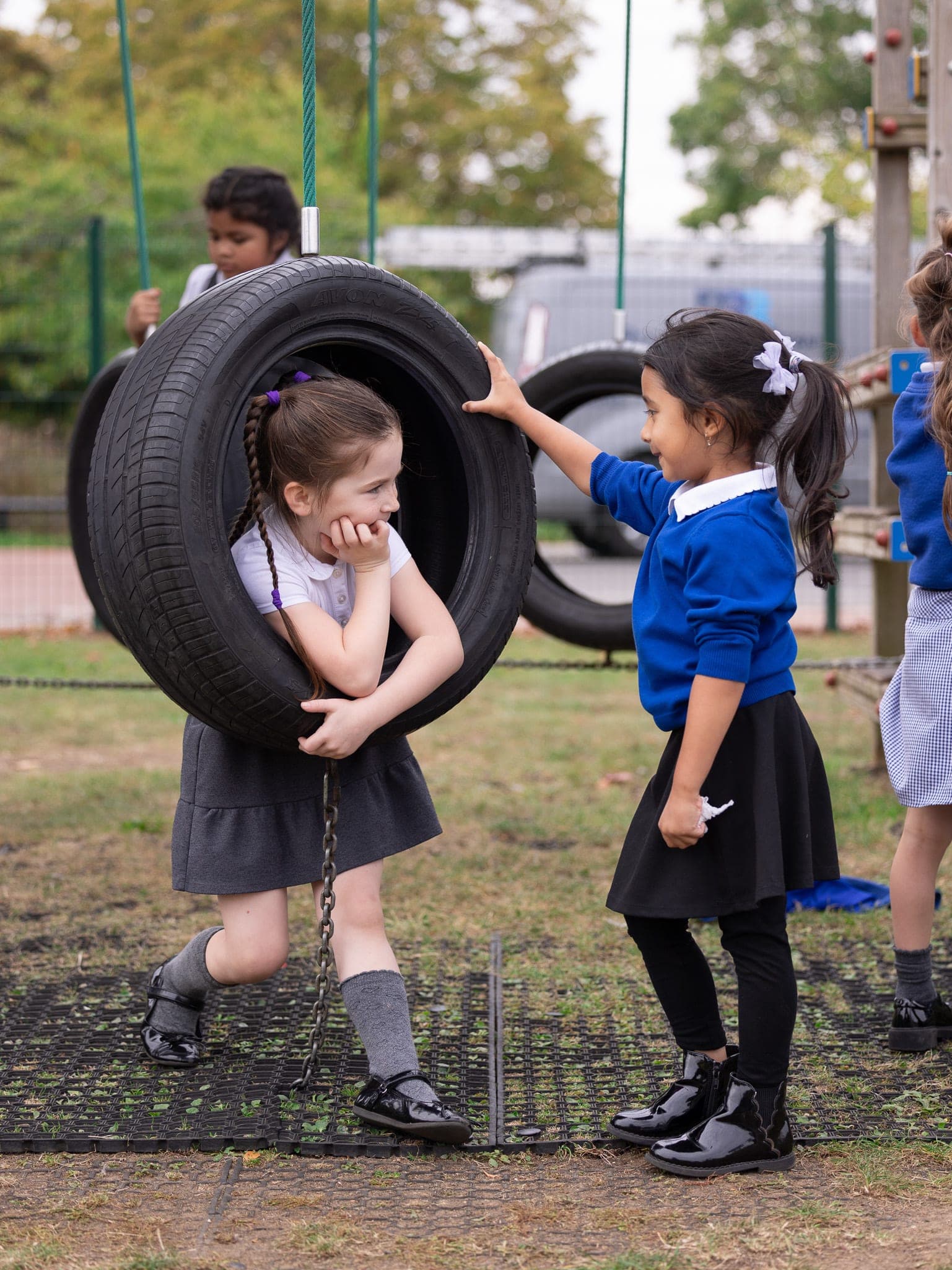 Two young pupils playing on a tyre swing in the playground