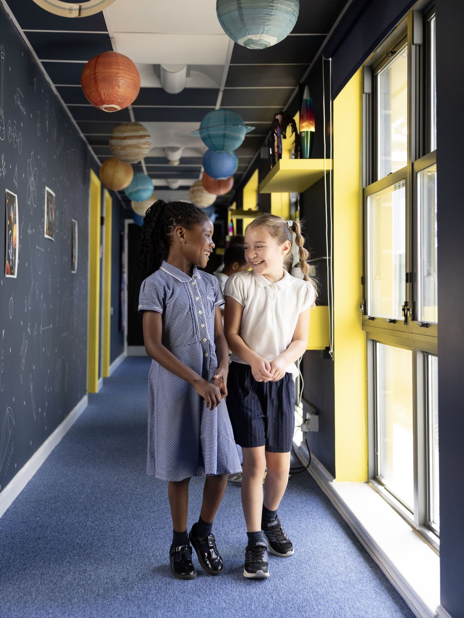 Two girls laughing together in a space-themed school corridor