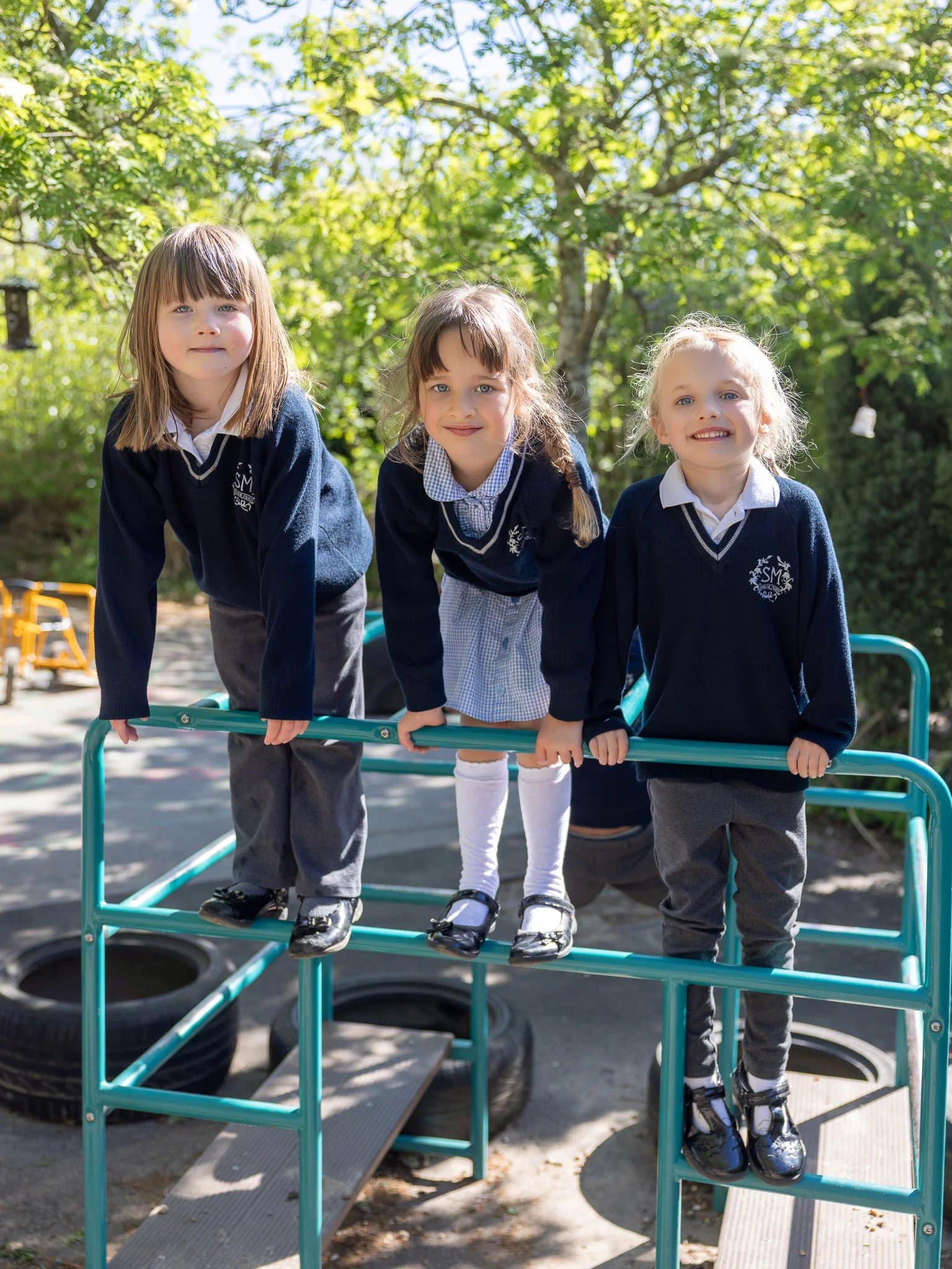 Three Reception girls smiling as they climb on the playground frame