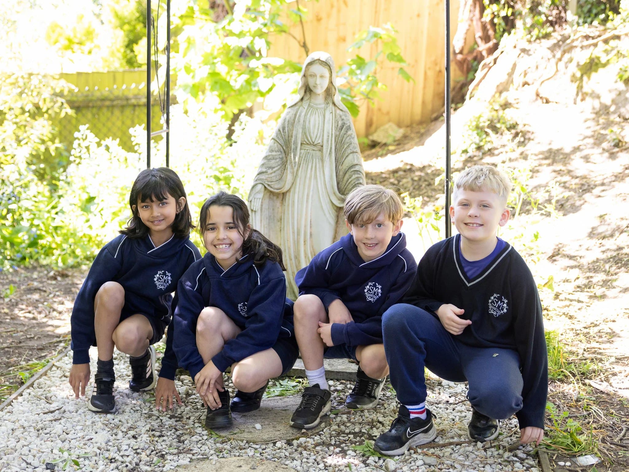 Four smiling pupils crouching in front of the statue of Our Lady in the school garden