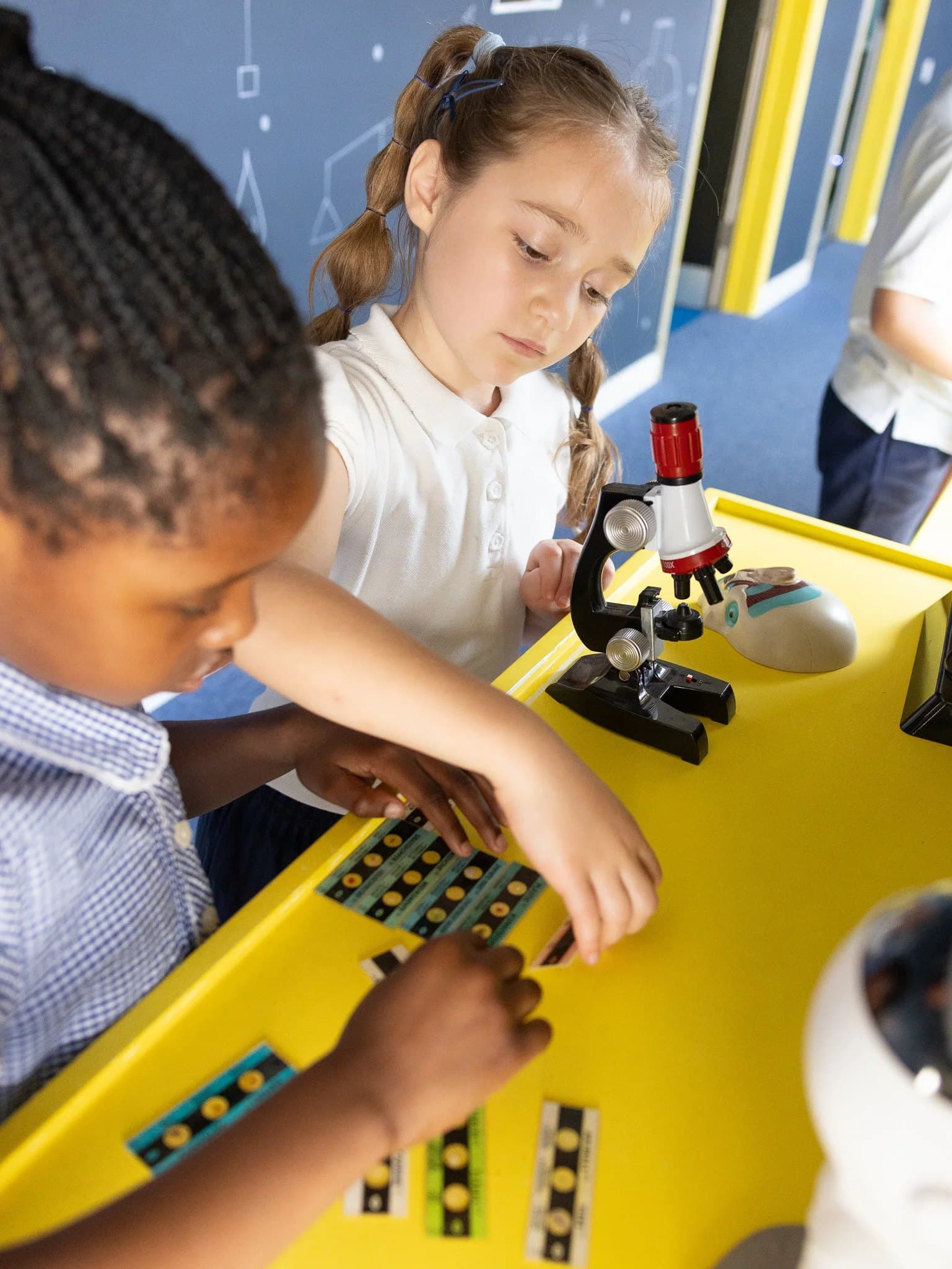 Two pupils exploring slides and a microscope at a science table