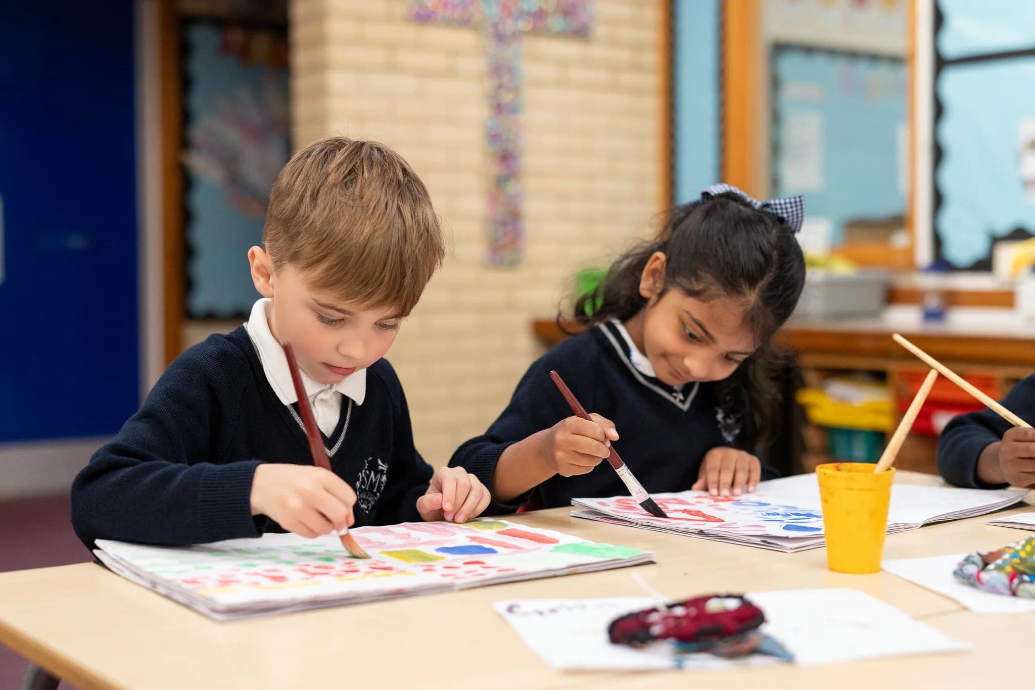 Two young pupils painting colourful patterns at their table