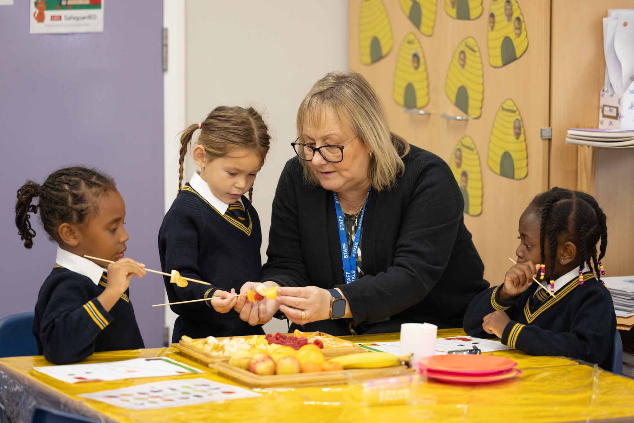 A teacher making fruit kebabs with young children