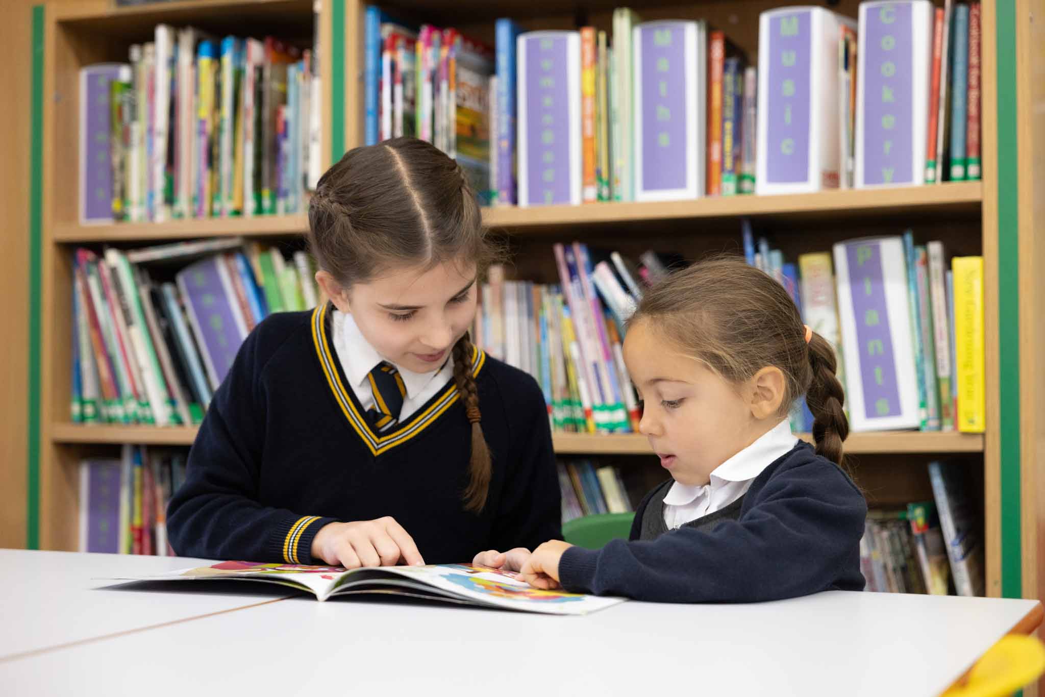 Two girls reading together in front of the library shelves