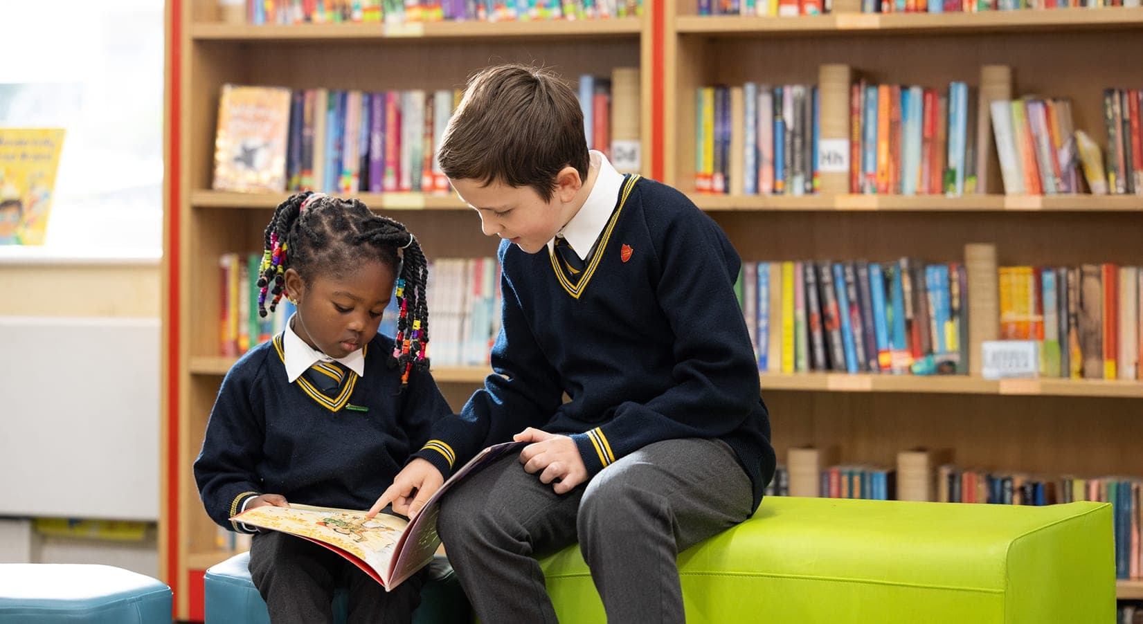 An older boy and a younger girl sharing a book in the school library