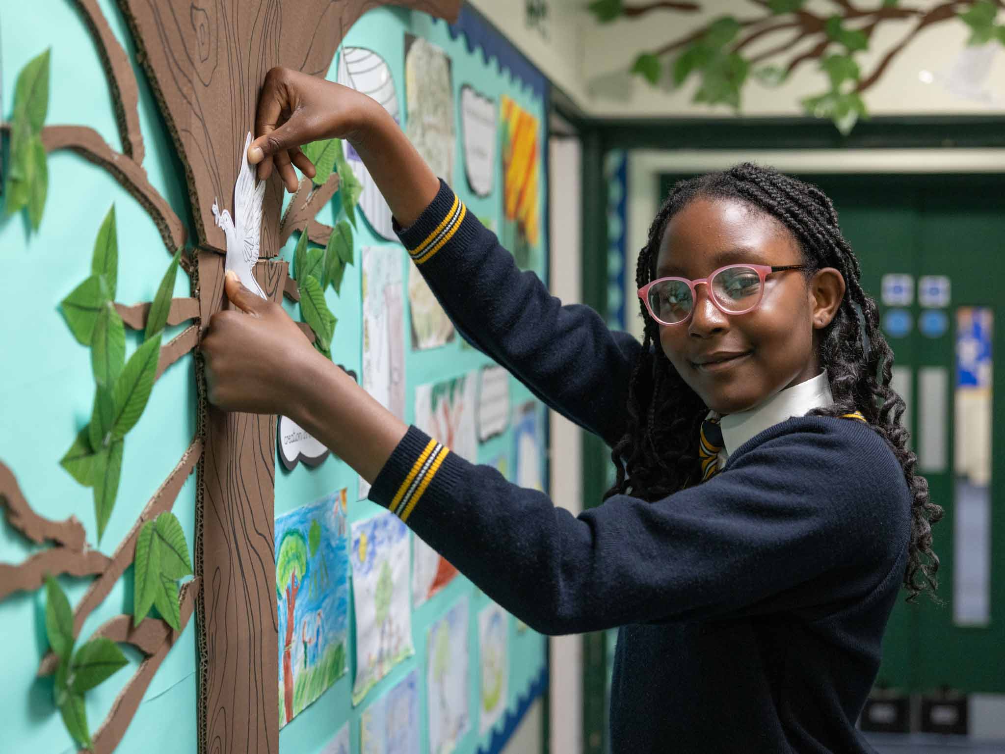 A girl putting up her work on a classroom display tree