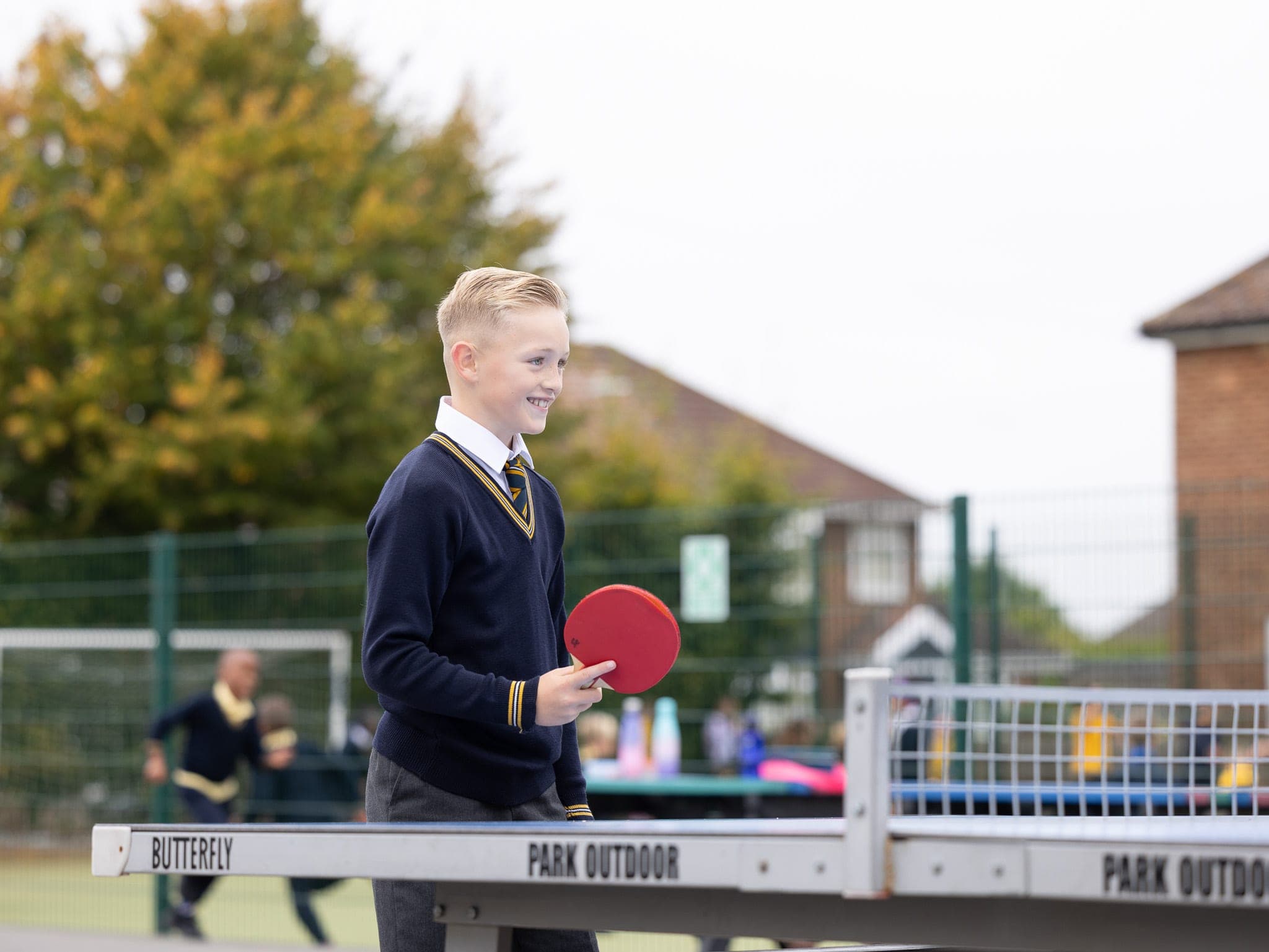 A smiling boy playing table tennis on the outdoor table at playtime