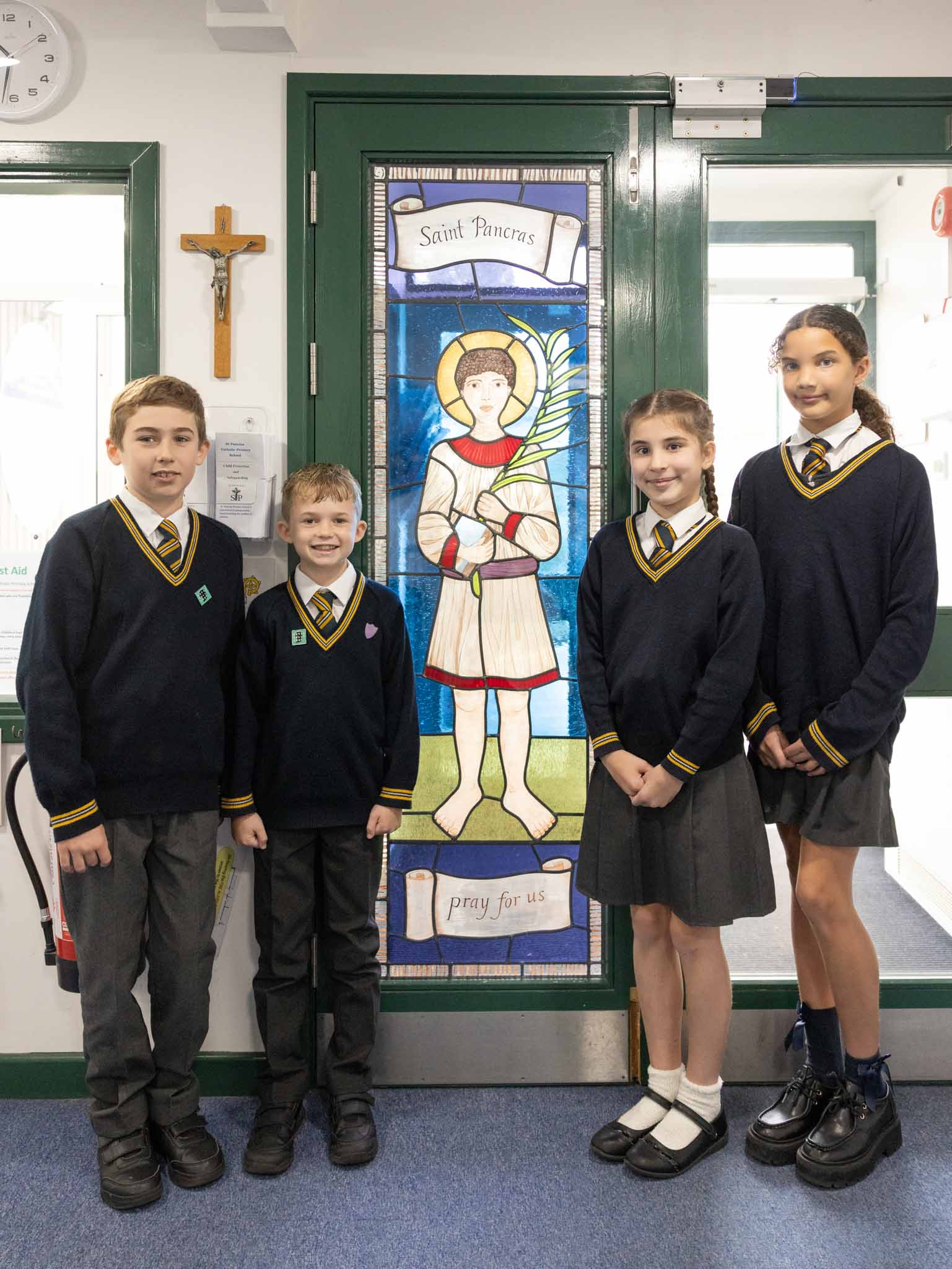 Four pupils standing beside the school's stained glass window of Saint Pancras