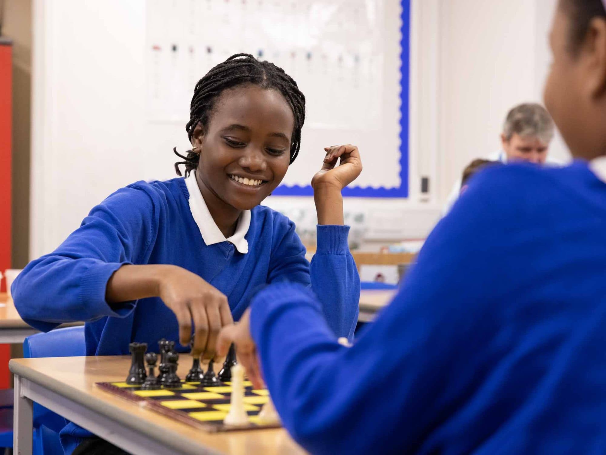 Girl in school uniform smiling as she plays chess