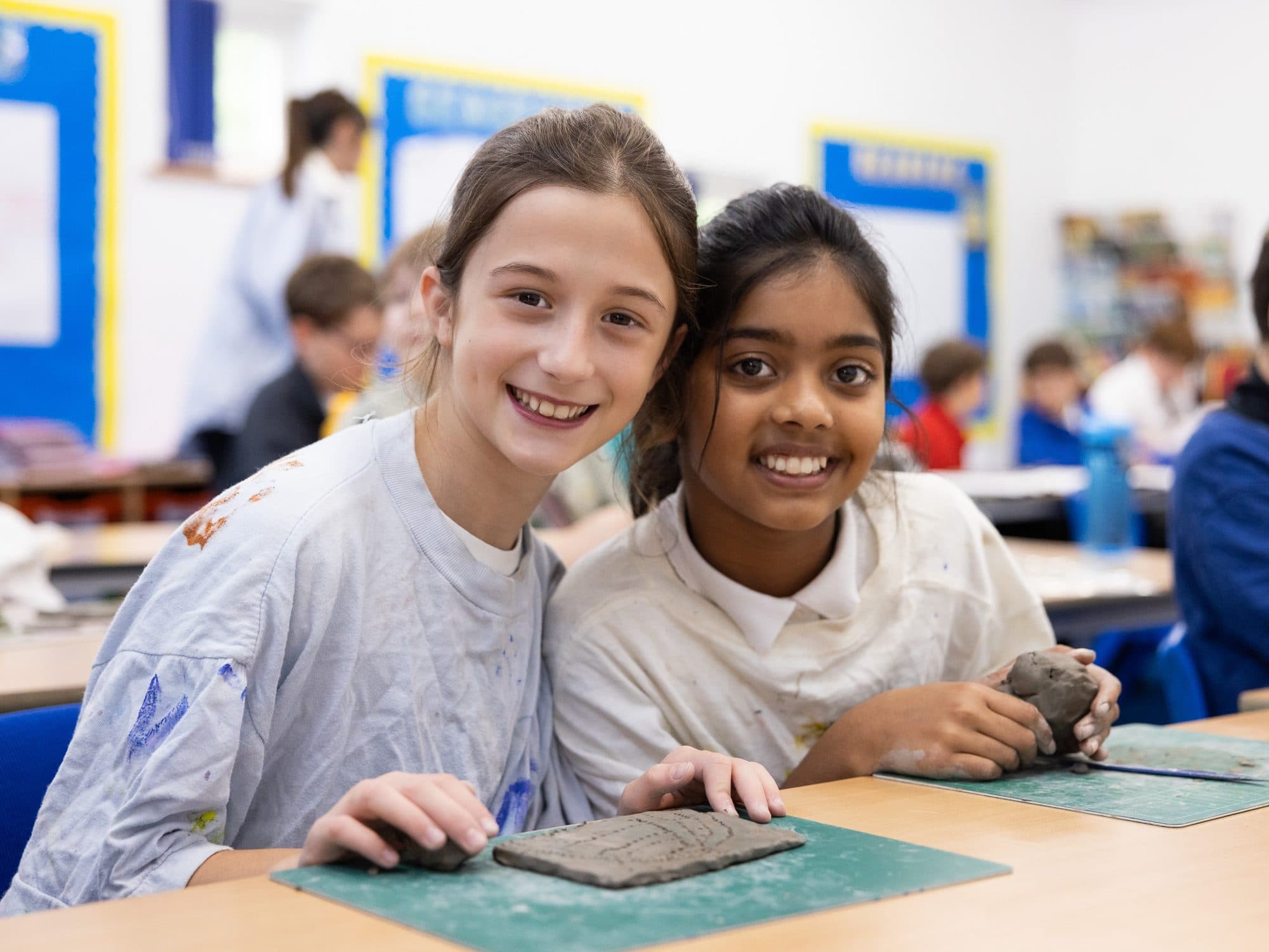 Two girls in art shirts smiling together over their clay work