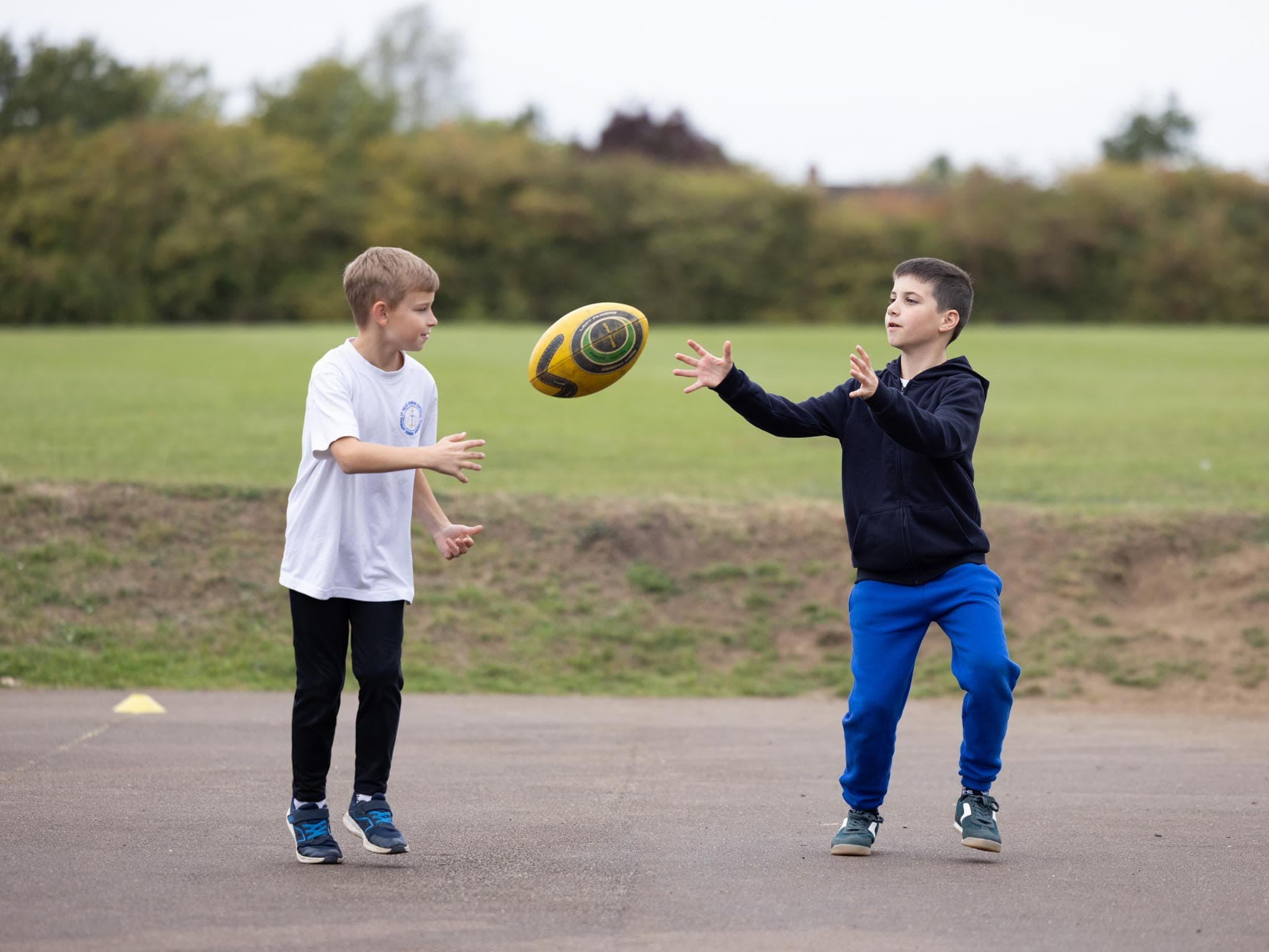 Two boys throwing a rugby ball on the playground beside the school field