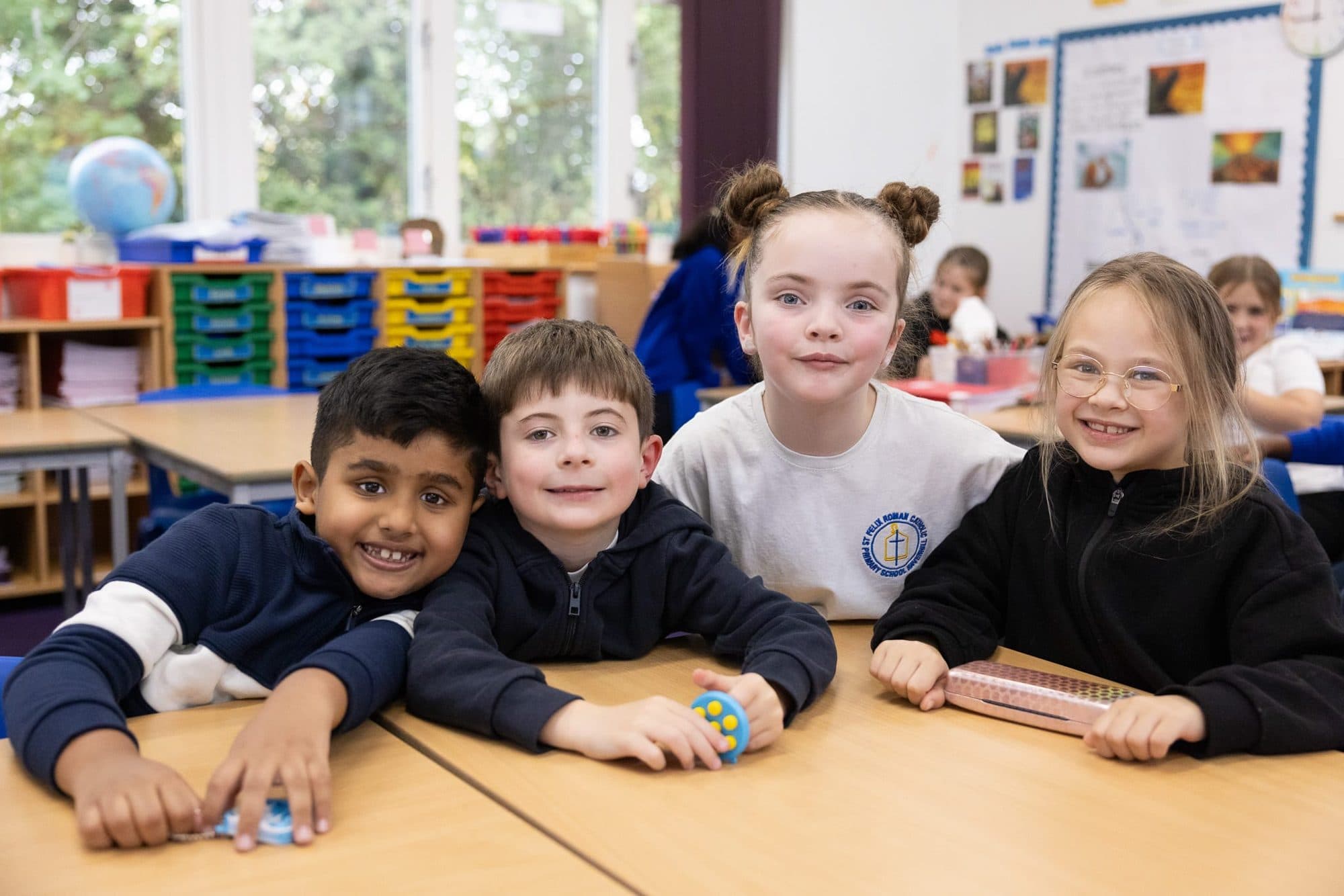 Four children grinning together at their classroom desks