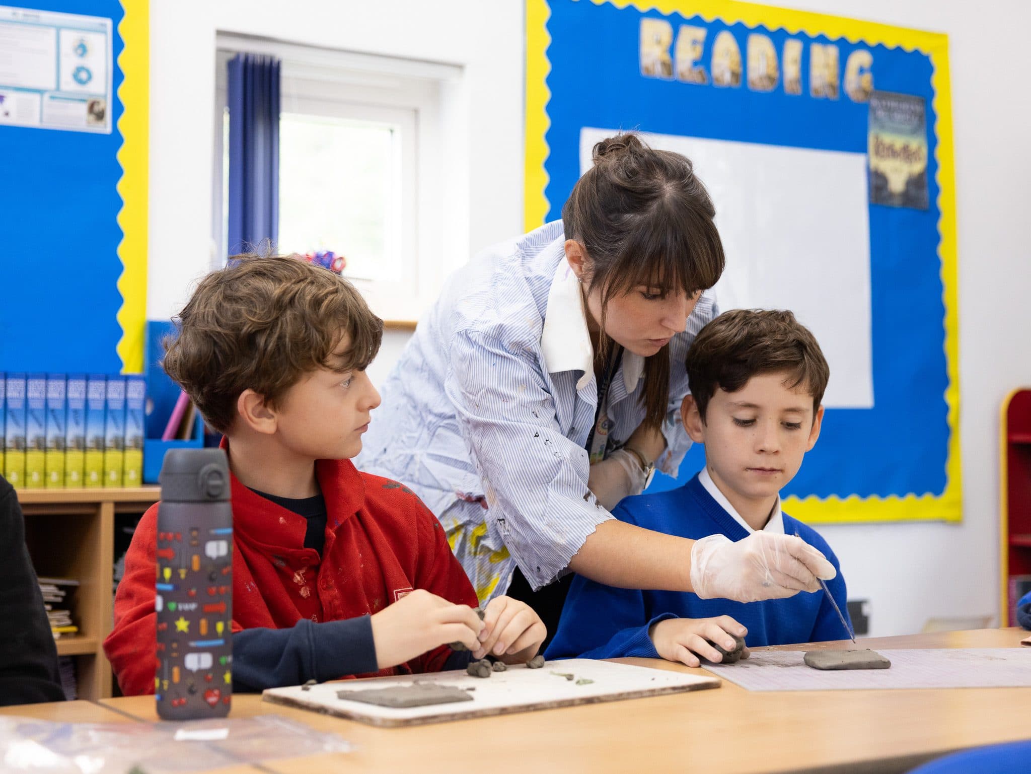Teacher helping two boys model clay tiles at their classroom table