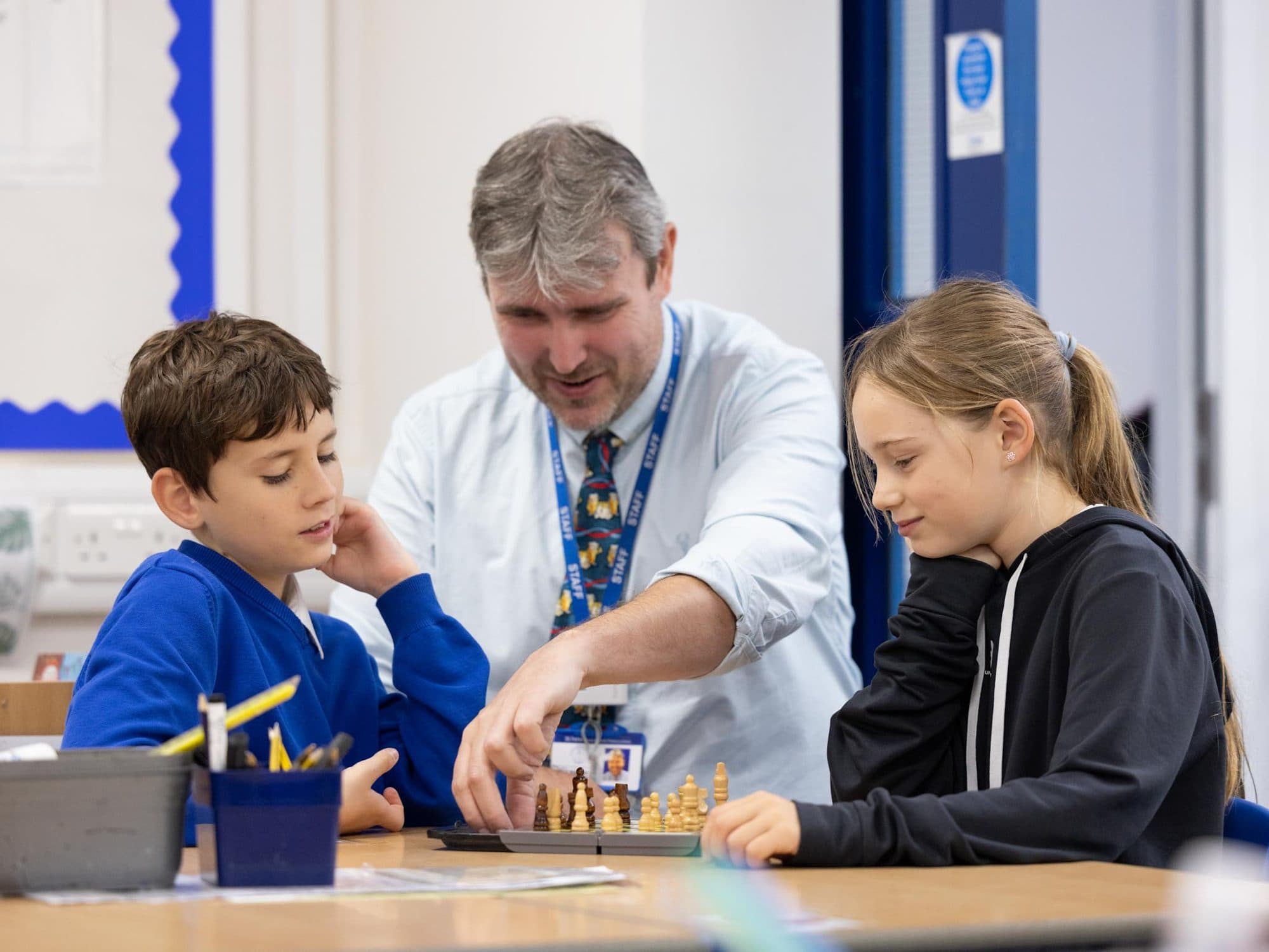 Teacher playing chess with two junior pupils