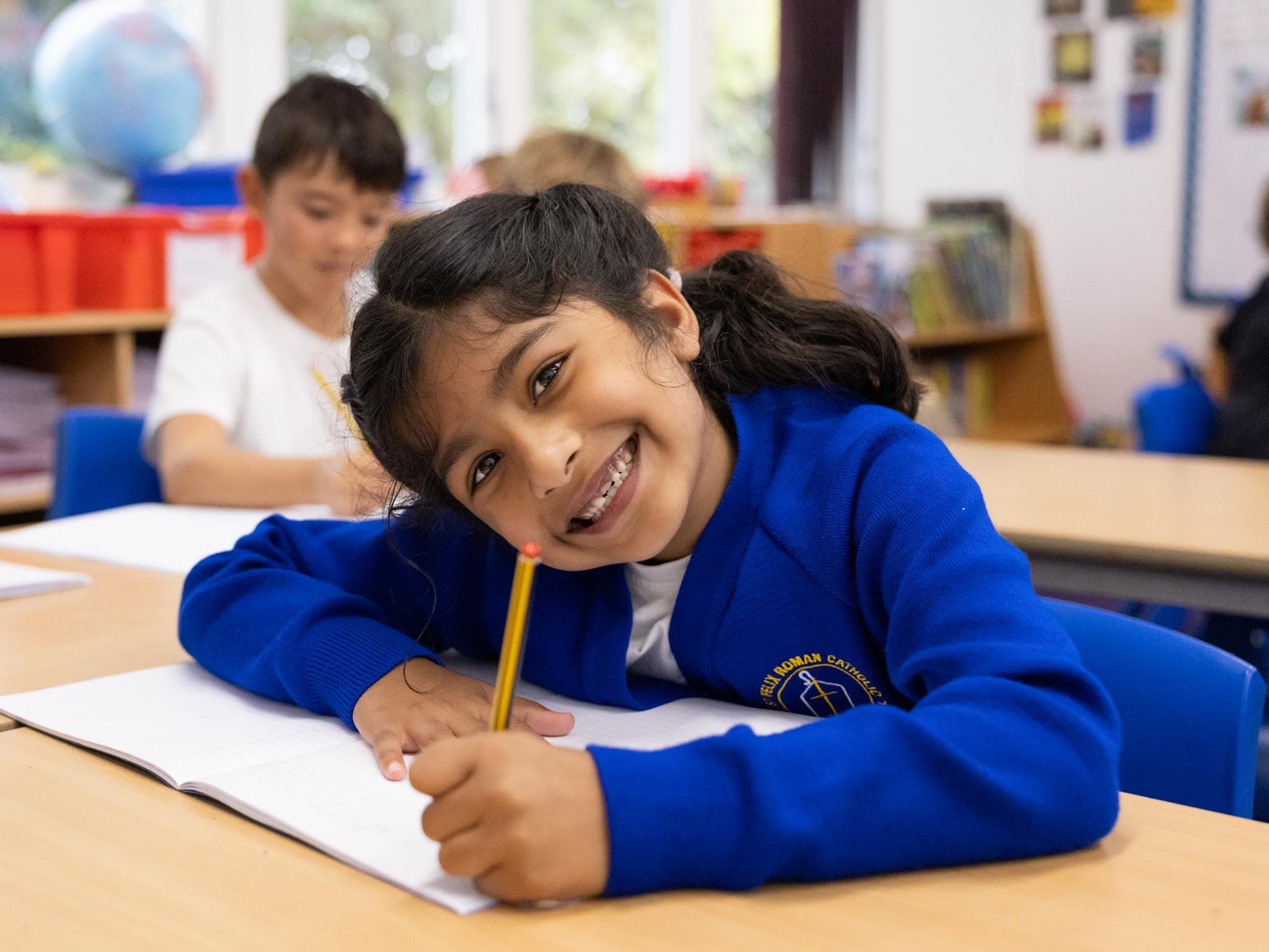 Smiling girl in a blue St Felix jumper resting her head on her hand while writing